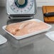 A white CKF foam meat tray with raw chicken breast on a scale.