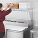 A person in a red apron using an Avantco stainless steel single deck overshelf to prepare food on a counter.