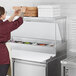 A woman in a red apron using an Avantco stainless steel single deck overshelf to prepare food on a counter.