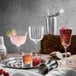 A variety of Luigi Bormioli Bach beverage glasses on a table filled with brown and pink drinks.