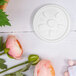 A white plastic disc with a vented lid design next to a white object with pink flowers.