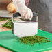 A person using a Nemco mezzaluna cutter to chop herbs on a cutting board.