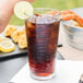 A Libbey wavy cooler glass of brown liquid with ice and a lime wedge on top.