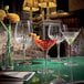 A group of Luigi Bormioli Mixology coupe glasses on a table with a vase of flowers.