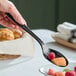 A black heavy-duty disposable serving spoon being used to serve fruit.
