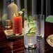 A Luigi Bormioli Elixir highball glass filled with a cocktail and a cucumber garnish on a table with a group of drinks.