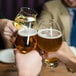 A group of people clinking Luigi Bormioli Birrateque wheat glasses filled with beer.