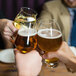 A group of people toasting with Luigi Bormioli Birrateque hard cider glasses full of amber liquid.