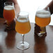 A group of Luigi Bormioli Birrateque hard cider glasses on a table with foamy liquid in one glass.