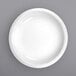 A close-up of a white International Tableware porcelain serving bowl with a white rim on a gray surface.