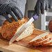 A person in black gloves using a Dexter-Russell scalloped bread knife to cut a loaf of bread.