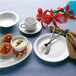 A white European white porcelain saucer on a table with plates and utensils.