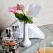 A white CAC European porcelain bud vase on a table with pink flowers in it.