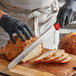 A person in black gloves using a Dexter-Russell scalloped bread knife to cut a loaf of bread on a cutting board.