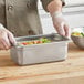 A person using a Choice stainless steel steam table pan to hold food.