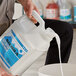 A person pouring Sierra by Noble Chemical floor finish from a white jug into a bucket.