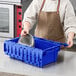 A woman in an apron putting a silver bowl into a blue Orbis tote box.