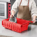 A woman in an apron putting a pan in a red Orbis tote box.