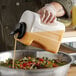 A person pouring a liquid into a bowl of salad from a Carlisle plastic jug.