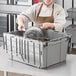 A woman in a chef's uniform using an Orbis Stack-N-Nest tote to store a pot.