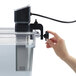 A hand holding a Hamilton Beach black sous vide immersion circulator over a fish tank.
