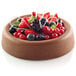 A chocolate tart with berries and mint leaves in a Silikomart silicone baking mold.