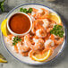 A plate of shrimp with Cocktail Sauce and lemon wedges.