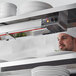 A chef in a white chef hat using a ServIt strip warmer in a professional kitchen.