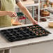 A black silicone baking mold with 24 donut-shaped compartments being filled with batter.