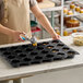 A black silicone baking mold with 24 round compartments for making muffins.