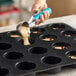 A black silicone baking mold with 24 compartments being filled with batter using a scoop.