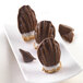 A plate of chocolate covered mini madeleine cookies on a white surface.