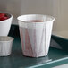 A tray of Genpak white paper souffle cups with a drink inside one.