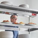 A man standing behind a shelf with plates of food using an Avantco strip warmer.