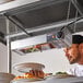 A man holding a plate of food under a ServIt strip warmer on a table in a professional kitchen.