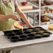 A black silicone baking mold with 15 square compartments being filled with batter.