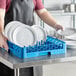 A man in an apron using a Carlisle dish rack to hold white plates on a counter.