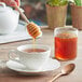 A person pouring Monarch's Choice Alfalfa Honey from a honey dipper into a cup of tea.