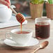 A spoon pouring Monarch's Choice buckwheat honey into a cup of tea.