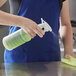 A person in a blue apron using a Bacoff spray bottle to disinfect a professional kitchen counter.