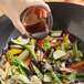 A hand pouring Lee Kum Kee Panda Brand oyster flavored sauce into a bowl of vegetables.