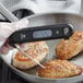 A person using a CDN DTF572 digital thermocouple to check the temperature of chicken in a pan.