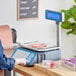 A digital price computing scale with a thermal label printer and LCD tower display being used to weigh sliced deli meat.