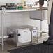 A man standing in a school kitchen next to a white Grease Guardian grease trap.