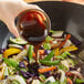 A hand pouring Lee Kum Kee Panda Brand Oyster Flavored Sauce into a bowl of food.