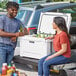 A man and woman sitting on the back of a truck with a white CaterGator cooler.