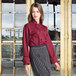 A woman in a Uncommon Chef burgundy long sleeve chef coat on a counter in a professional kitchen.