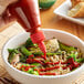 A hand pouring Lee Kum Kee Sriracha Chili Sauce onto a bowl of soup with vegetables.