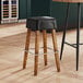 A Lancaster Table & Seating Sofia wood bar stool with a black vinyl seat