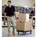 A man wearing a black shirt and khaki pants pushing a Rubbermaid Triple Trolley with boxes.